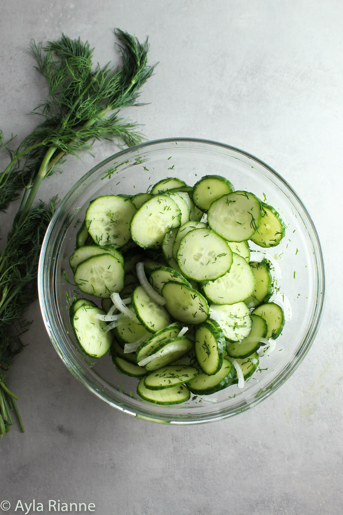 cucumber dill salad in a glass bowl with fresh dill behind it