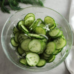 cucumber dill salad in a glass bowl with fresh dill behind it