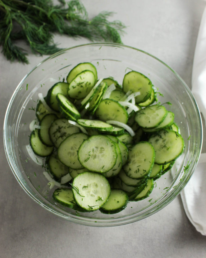 cucumber dill salad in a glass bowl with fresh dill behind it
