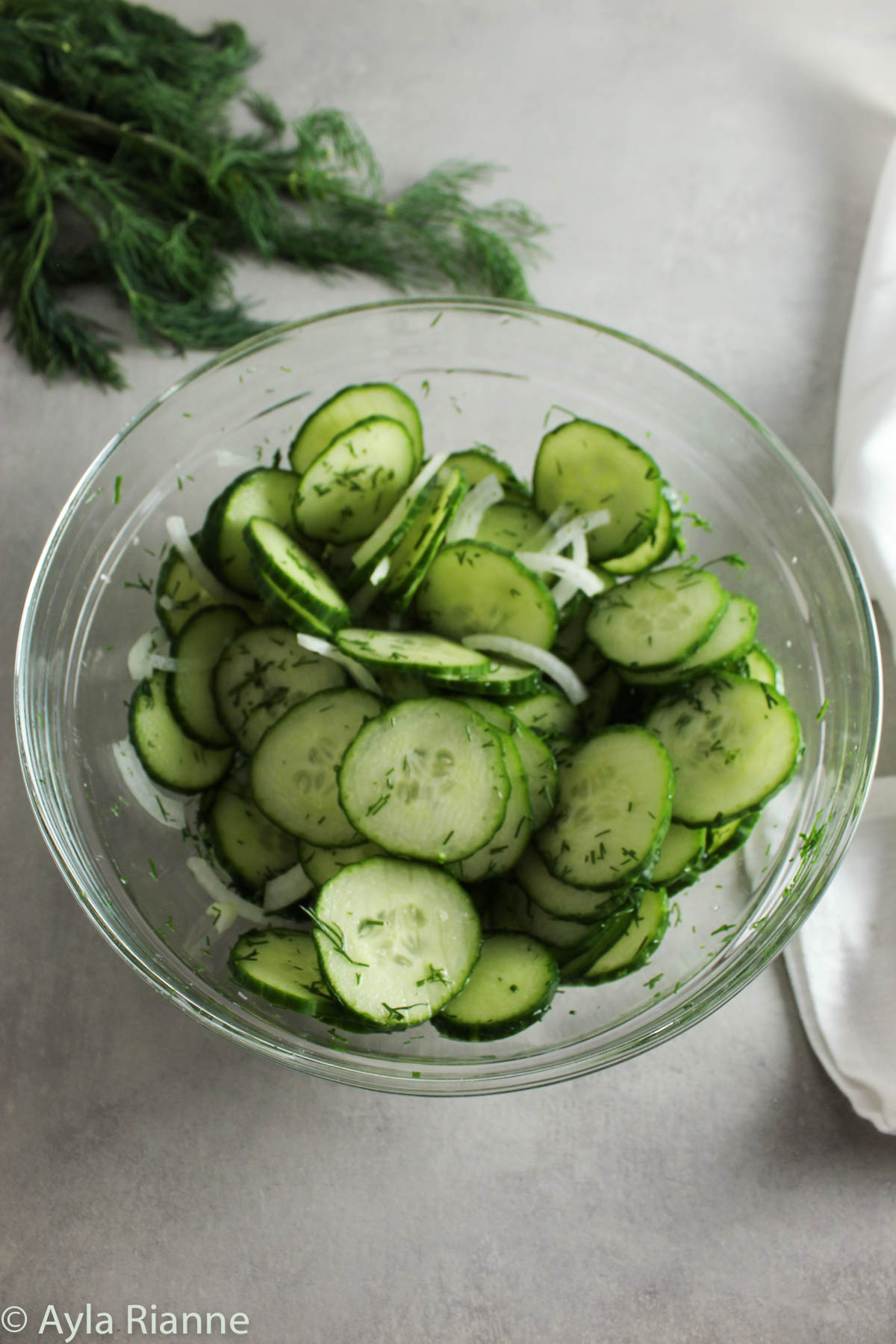 cucumber dill salad in a glass bowl with fresh dill behind it