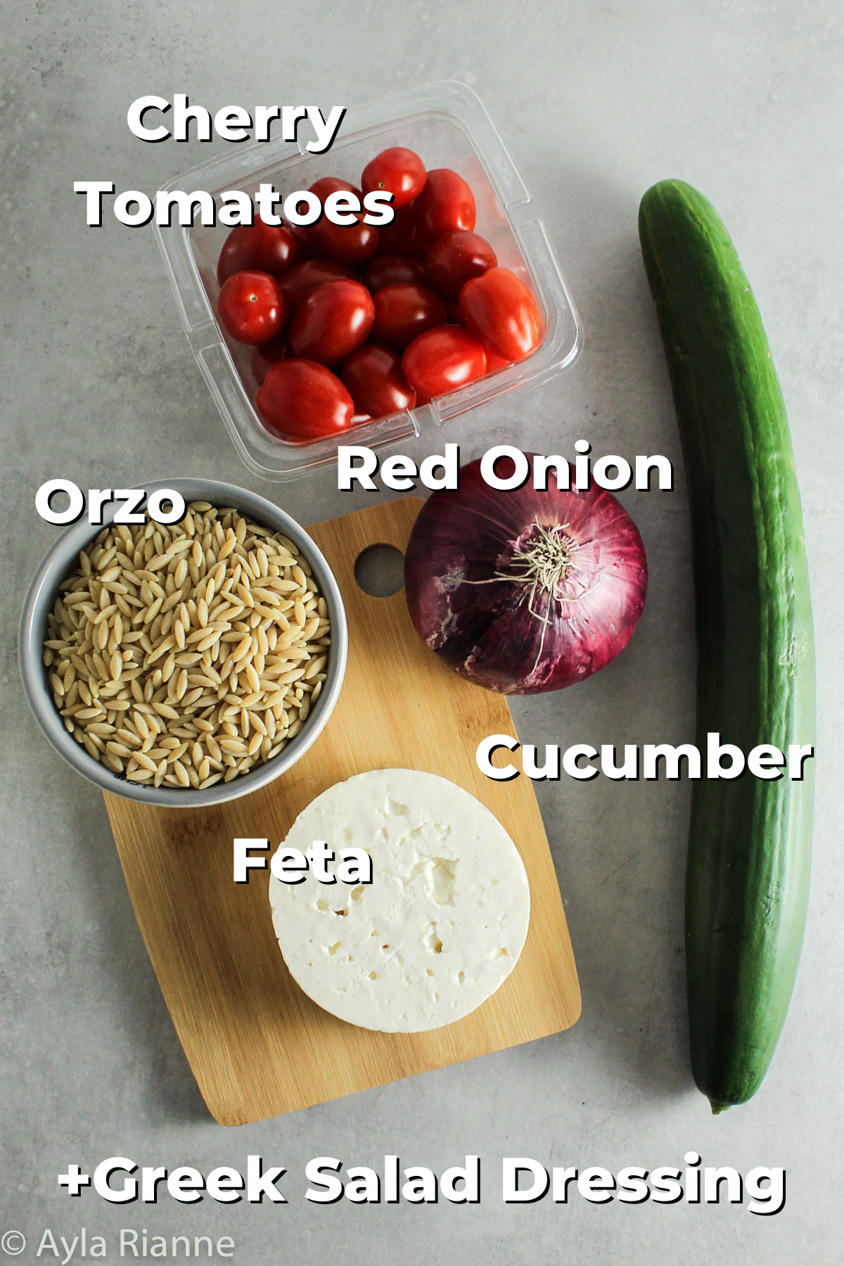 ingredients for greek orzo pasta salad on a counter including cherry tomatoes, red onion, cucumber, feta, and orzo