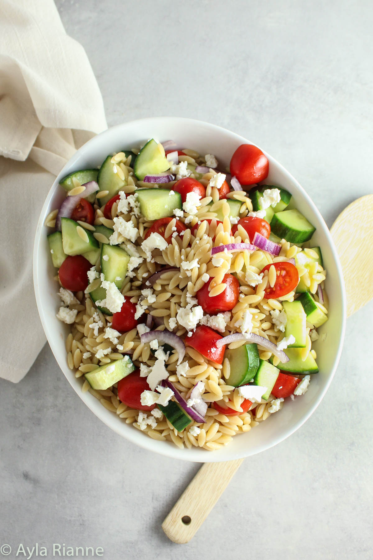 greek orzo pasta salad in a bowl with a towel and wooden spoon in the background