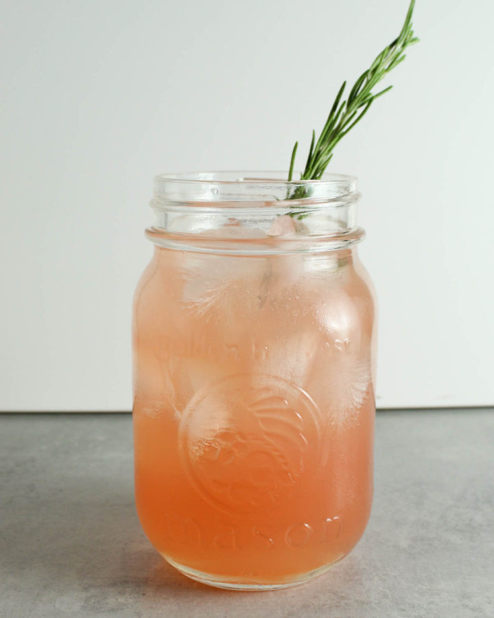 rosemary grapefruit drink in a mason jar with a rosemary sprig