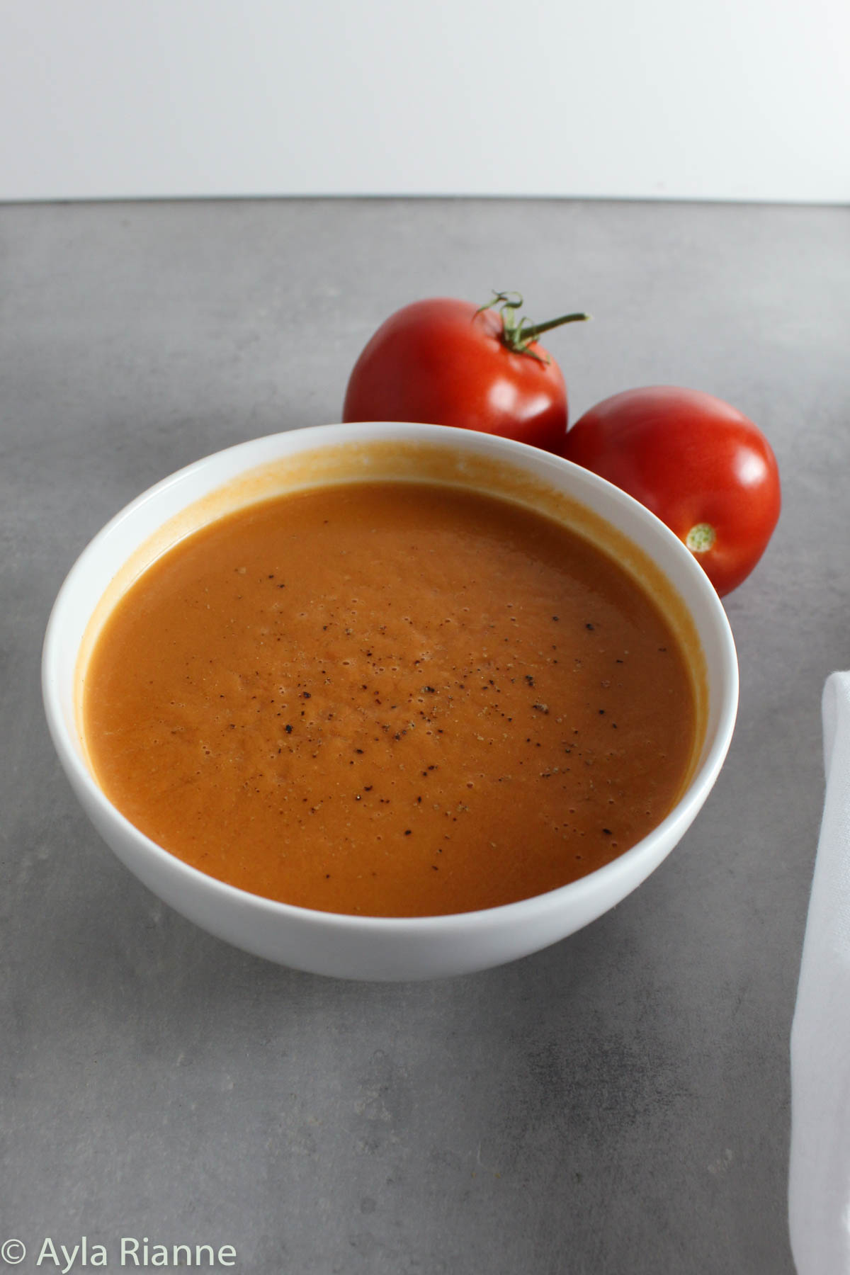 a bowl of tomato soup with 2 tomatoes in the background