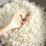 riced cauliflower in a frying pan with a wooden spoon