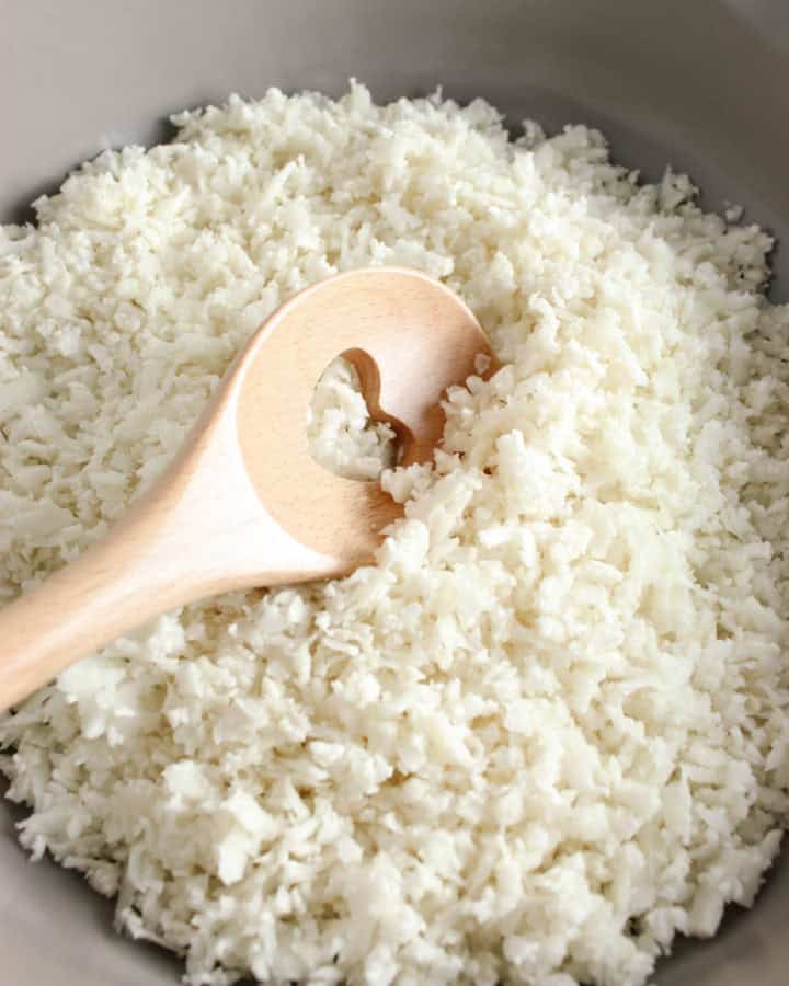 riced cauliflower in a frying pan with a wooden spoon