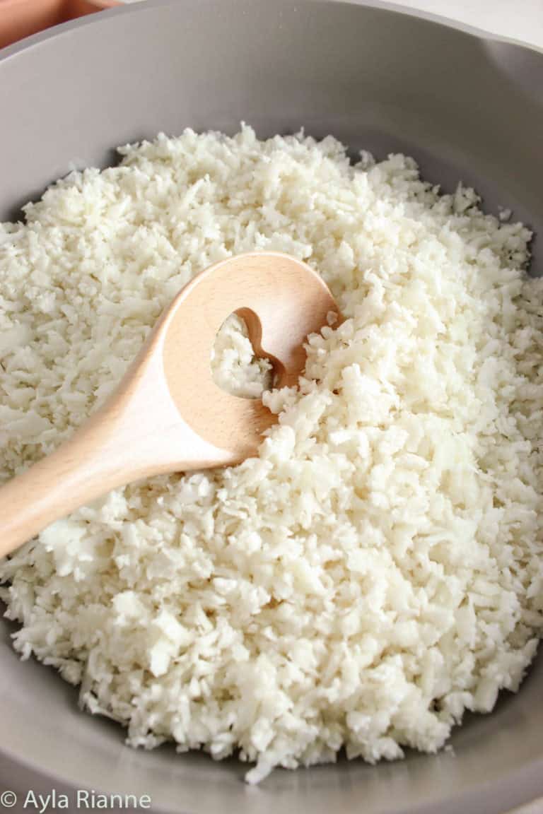 riced cauliflower in a frying pan with a wooden spoon