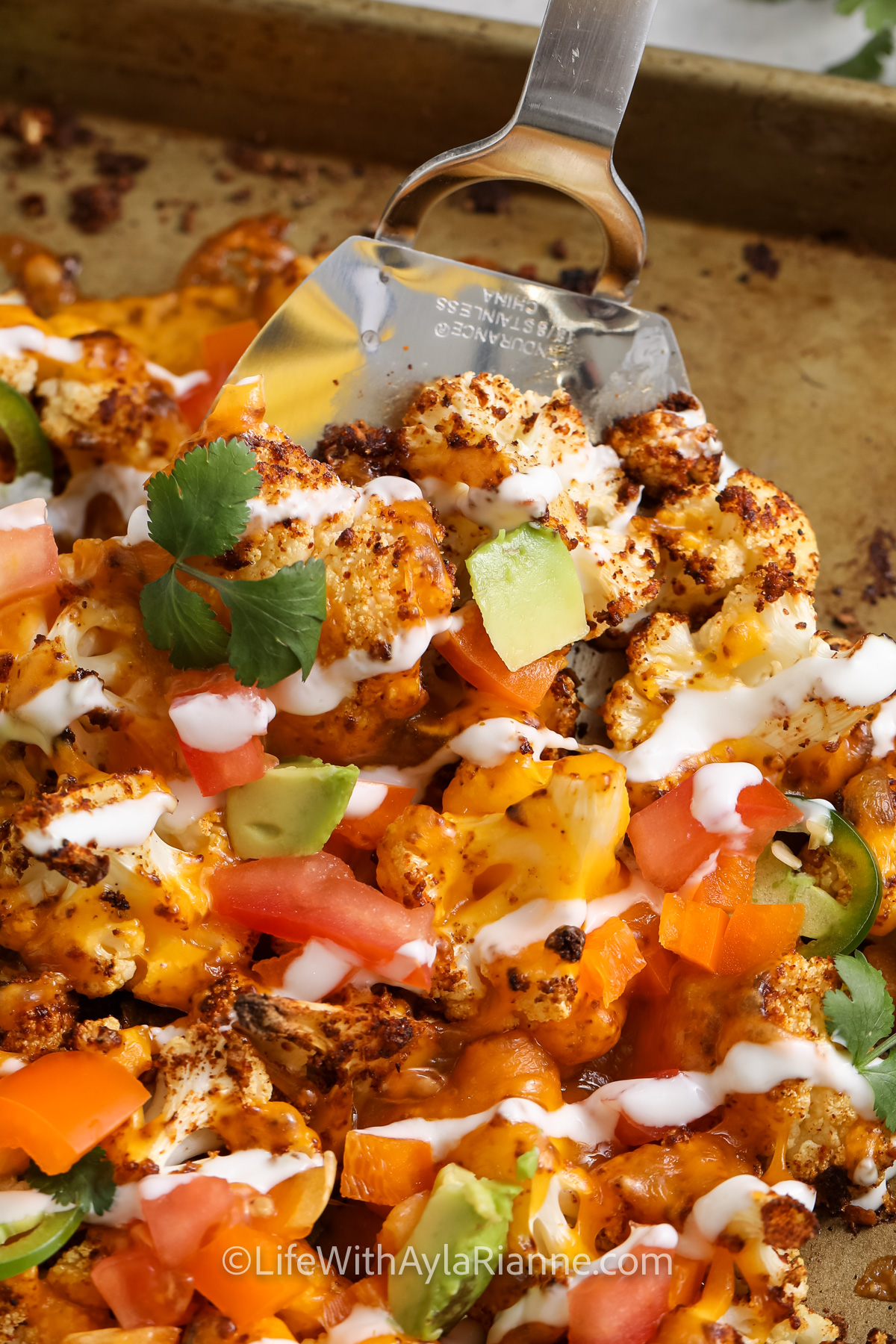 Cauliflower Nachos on a baking sheet with some being scooped up with a spatula