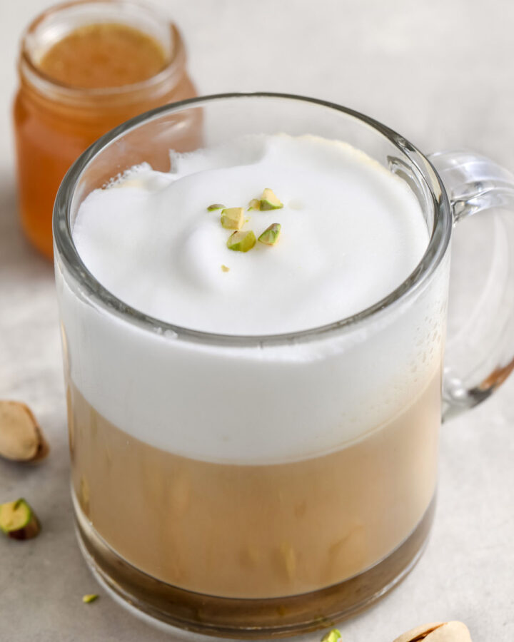 pistachio latte in a clear mug with pistachios on top as garnish
