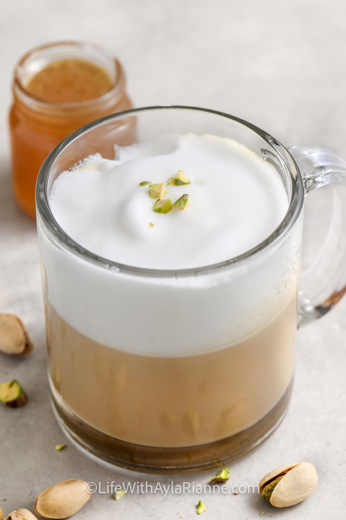 pistachio latte in a clear mug with pistachios on top as garnish