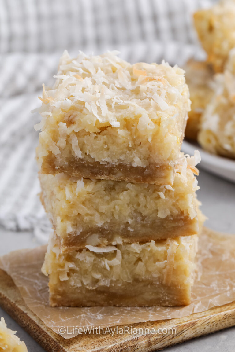 three coconut bars stacked on a cutting board