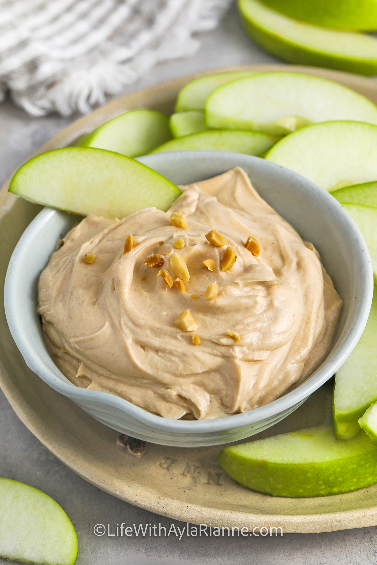 an apple dipping into the bowl of peanut butter dip with peanuts on top